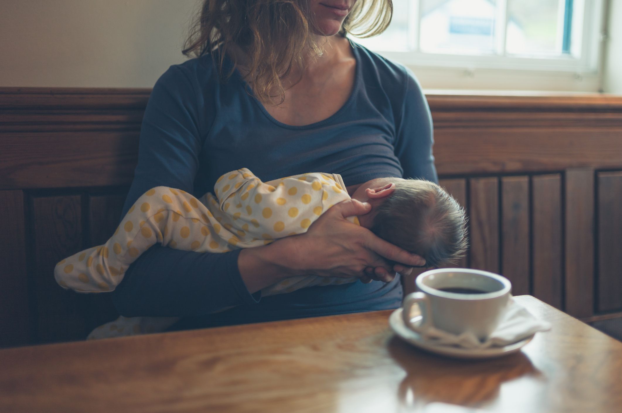 Mãe amamentando o filho em restaurante ao lado de xícara de café
