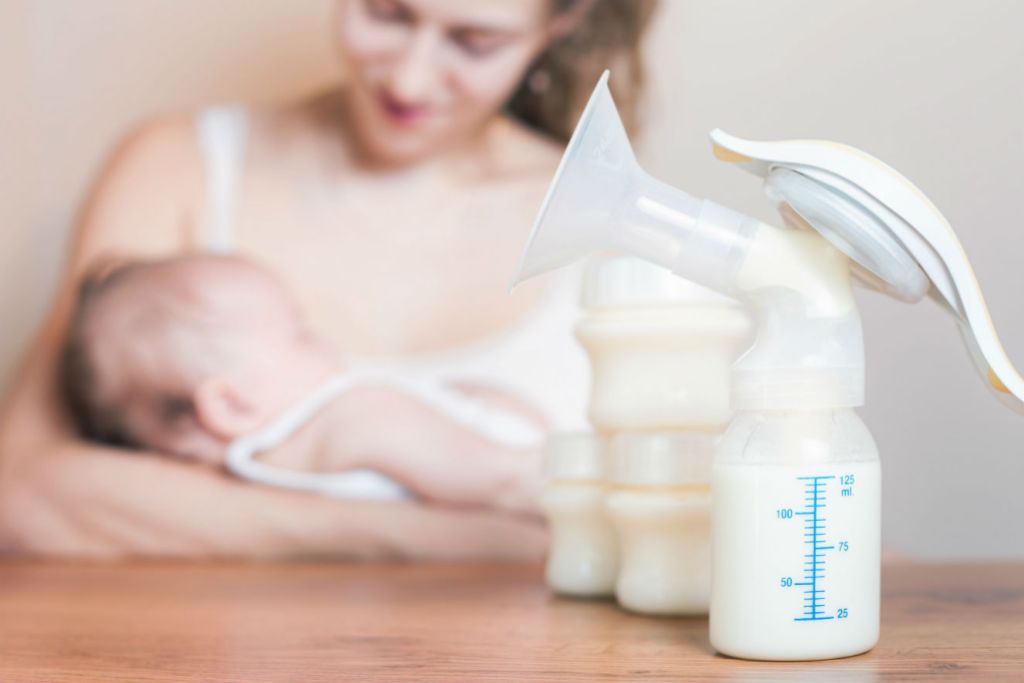 bomba de extração de leite materno em primeiro plano. Ao fundo, mulher amamenta bebê