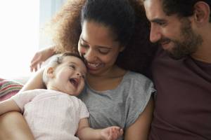 casal sorri enquanto olha para um bebê, que está no colo da mãe