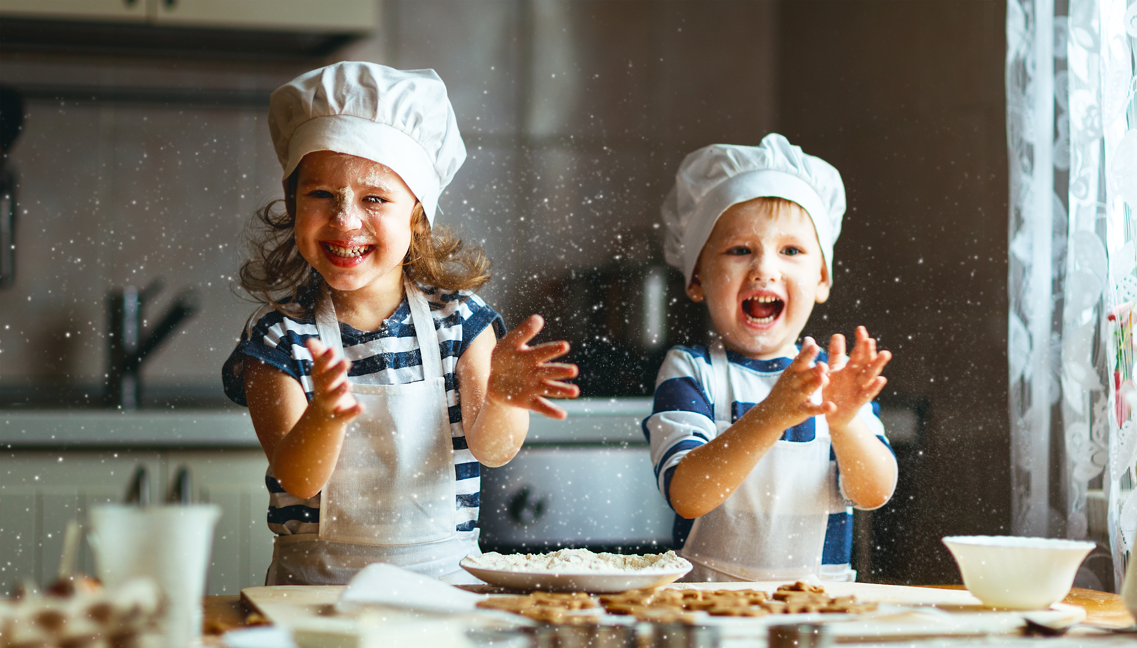 Crianças na cozinha preparando massa, usando avental branco e chapéu de chef