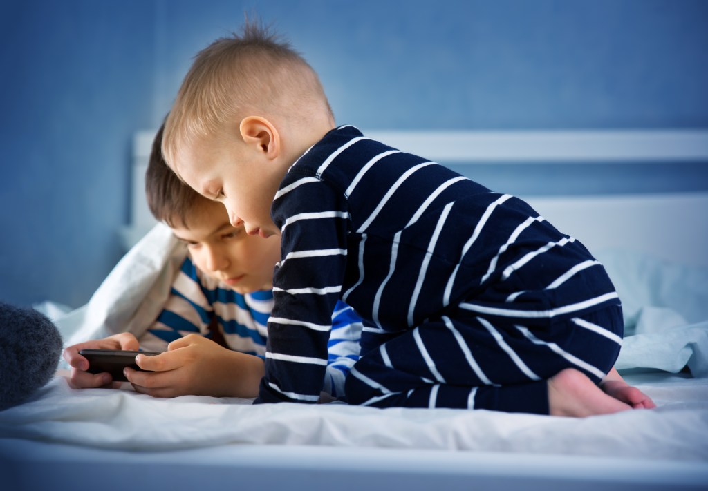 Dois meninos de pijama listrado na cama mexendo no celular