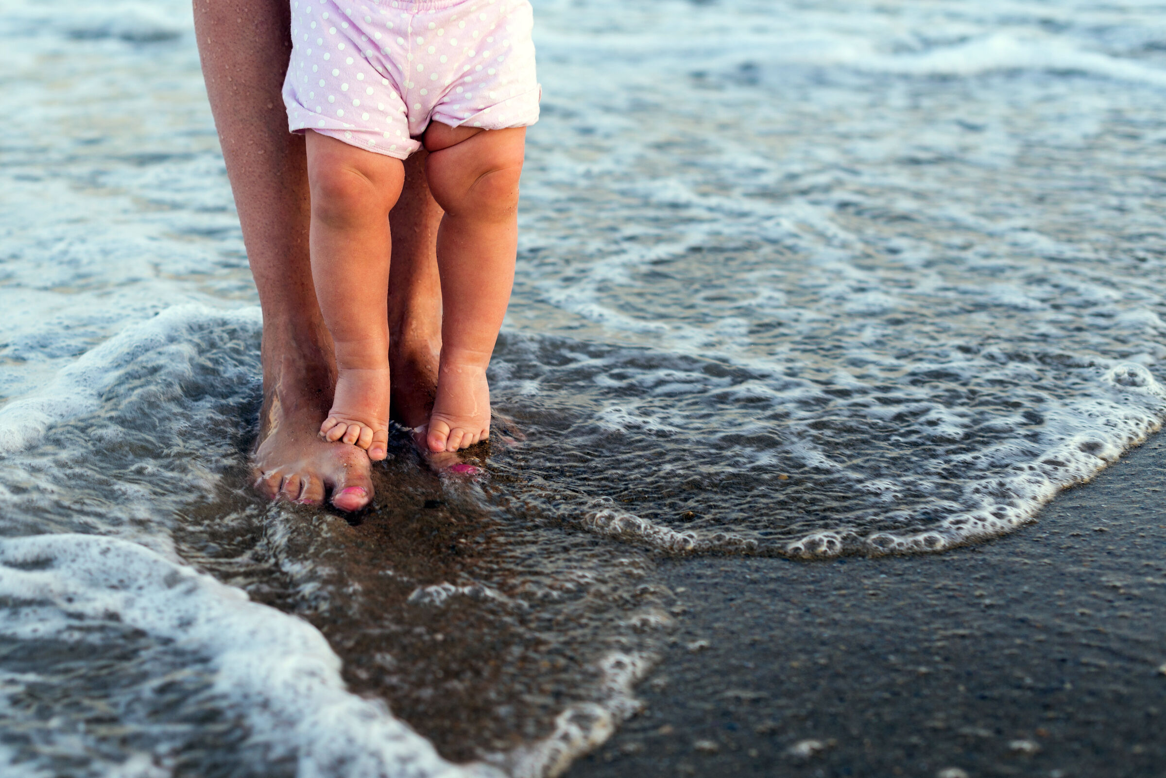 Mãe segurando bebê na praia - acidentes com crianças no verão