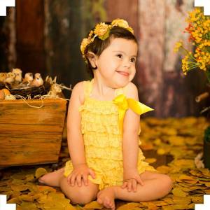 Garota de vestido amarelo e coroa de flores sentada no chão, sorrindo para a foto