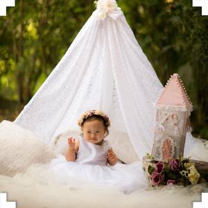 Recém-nascido de vestido branco, sentada em baixo de uma tenda branca em um ensaio fotográfico