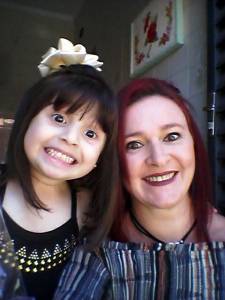 Filha de laço no cabelo, com a mãe ruiva de batom vermelho, posando para uma foto juntas