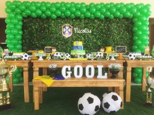 Decoração baseada em Copa do Mundo, com balões verde e amarelo, bolo em formato de bola