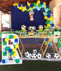 Decoração baseada em Copa do Mundo, com balões verde e amarelo, bolo em formato de bola