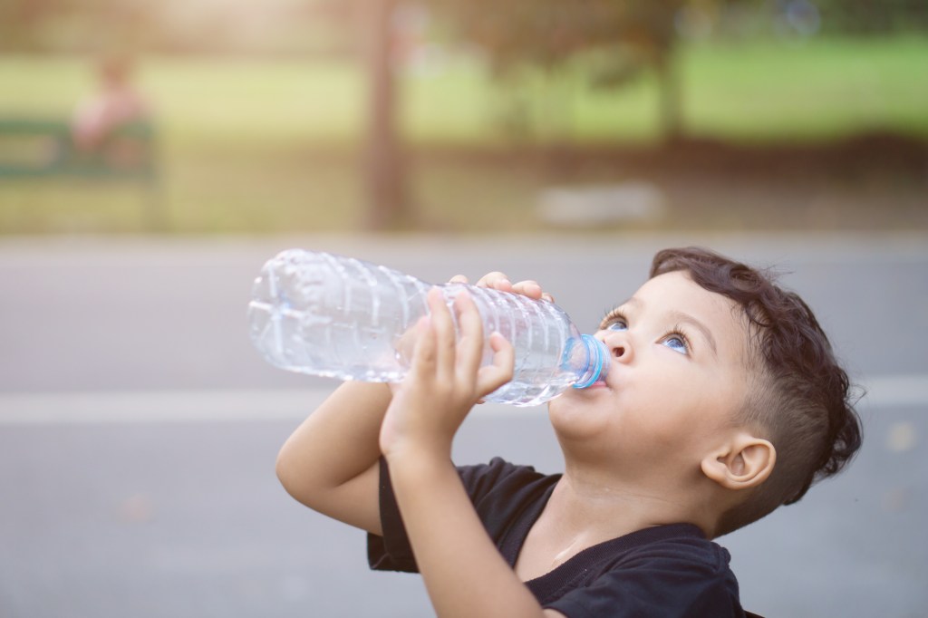 Criança bebendo água direto de uma garrafa plástica grande.