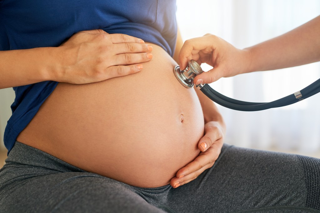 médico com estetoscópio encostado na barriga de uma mulher grávida