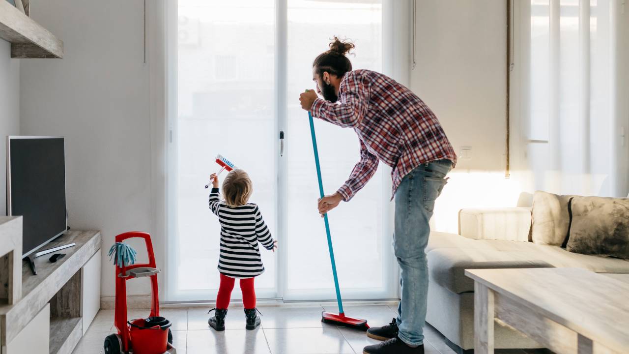 homem limpando o chão com um rodo e criança limpando um vidro com uma escova de brinquedo