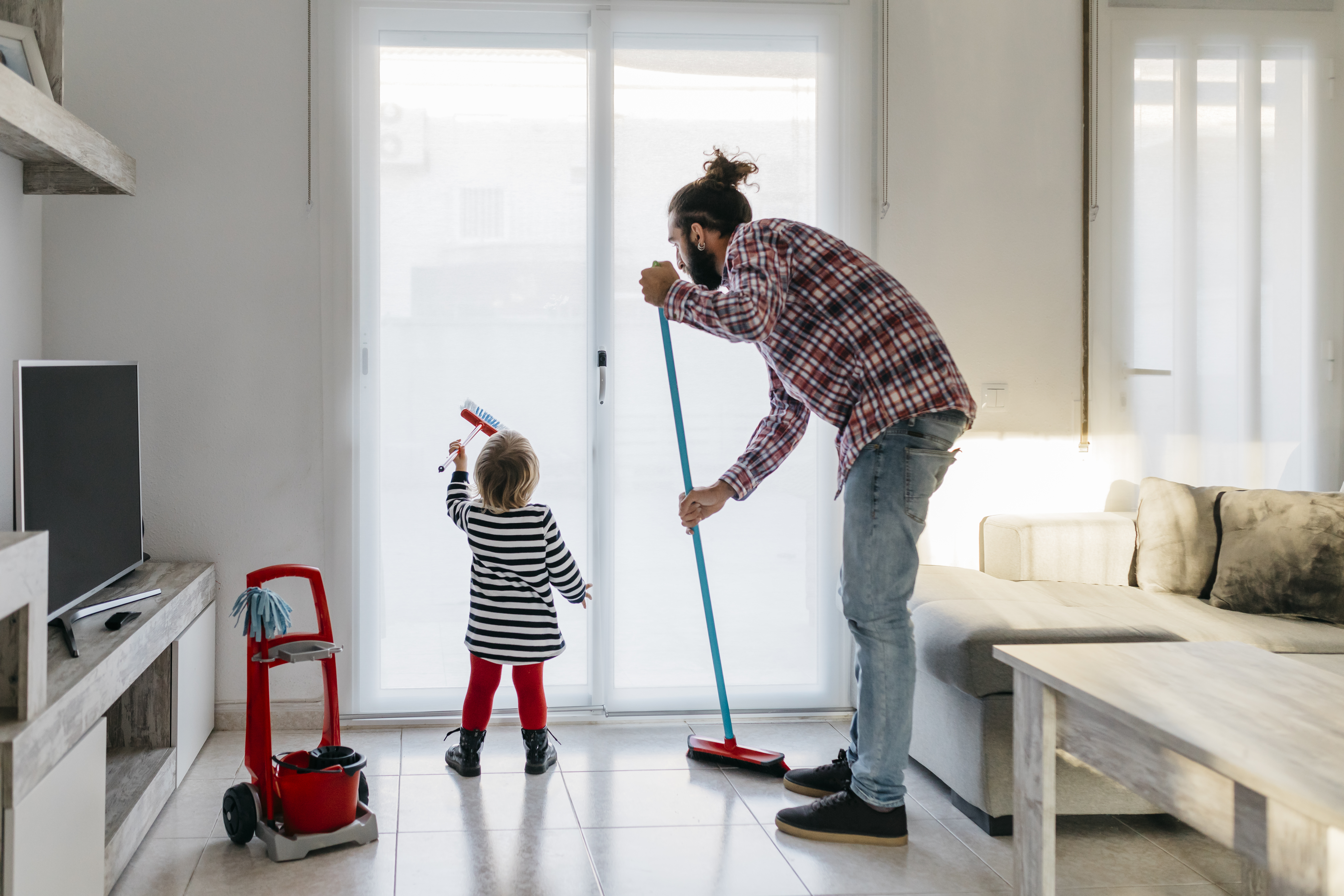 homem limpando o chão com um rodo e criança limpando um vidro com uma escova de brinquedo