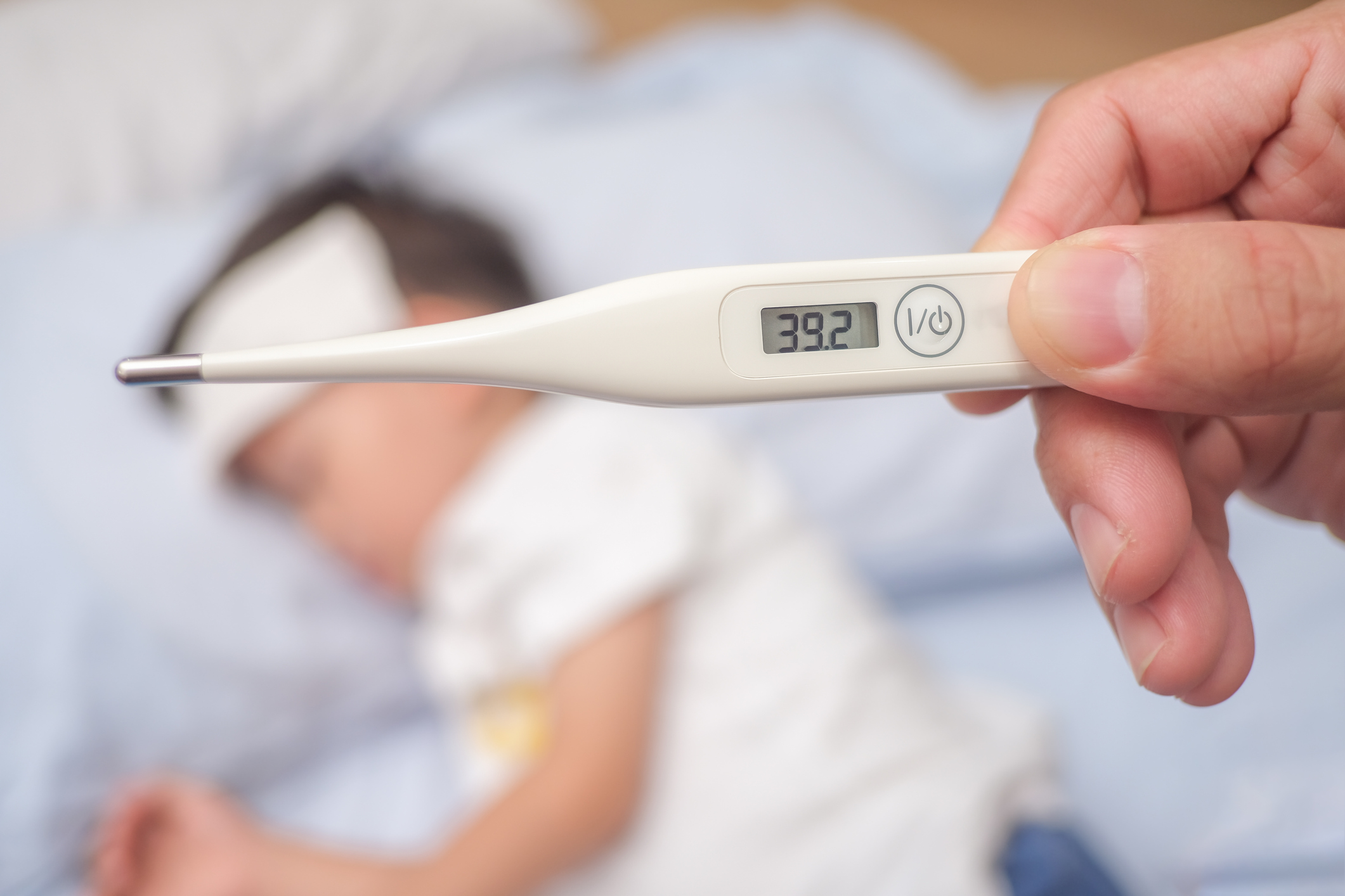 A thermometer marked 39.2 degrees is in hand.  In the background, out of focus, lies a child