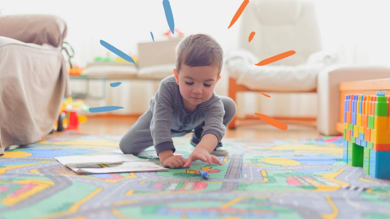 Menino, por volta de 3 anos, brincando sozinho ajoelhado no tapete colorido.