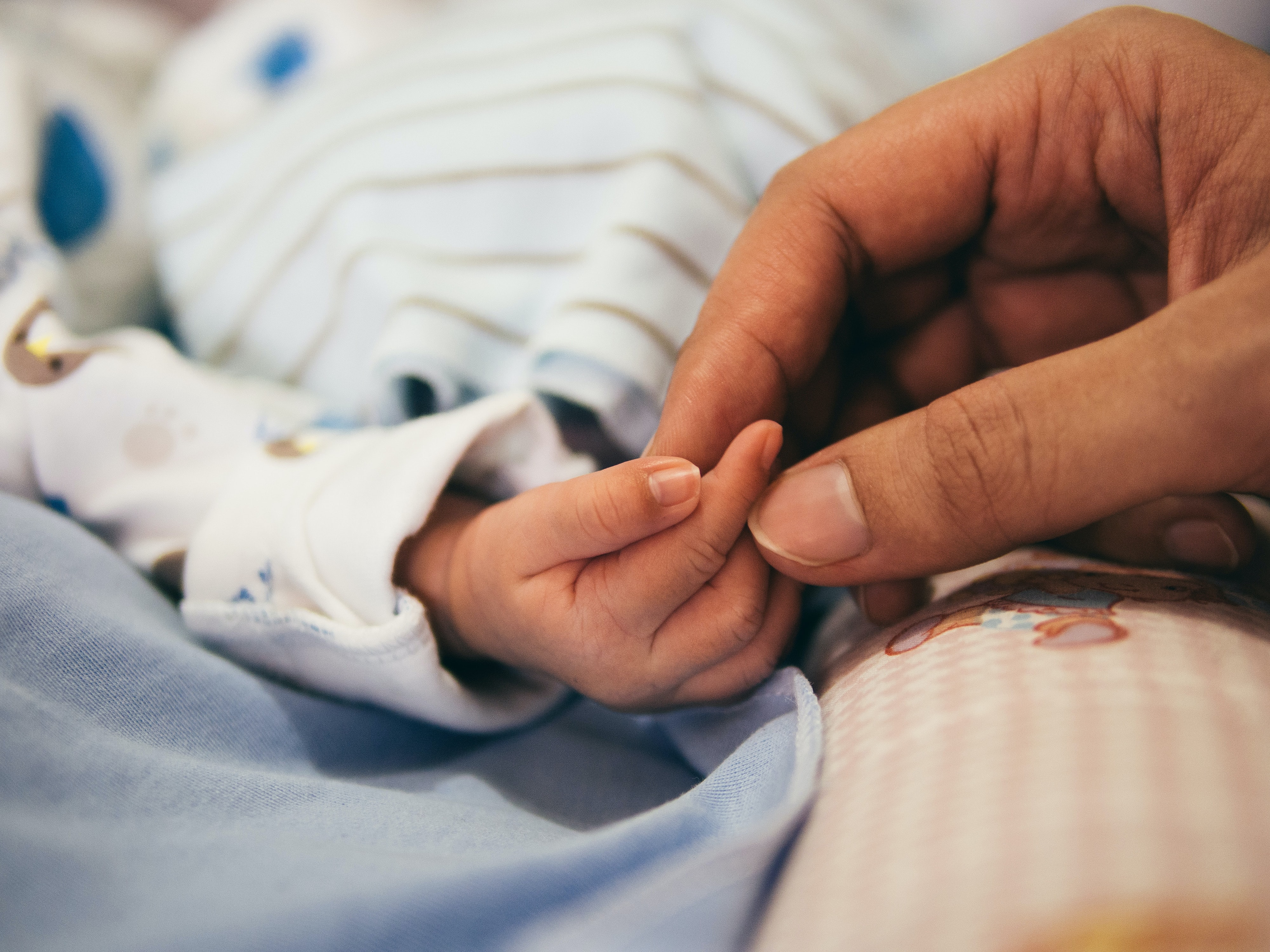 Mãe segurando a mão do bebê recém-nascido, ambos têm pele clara.