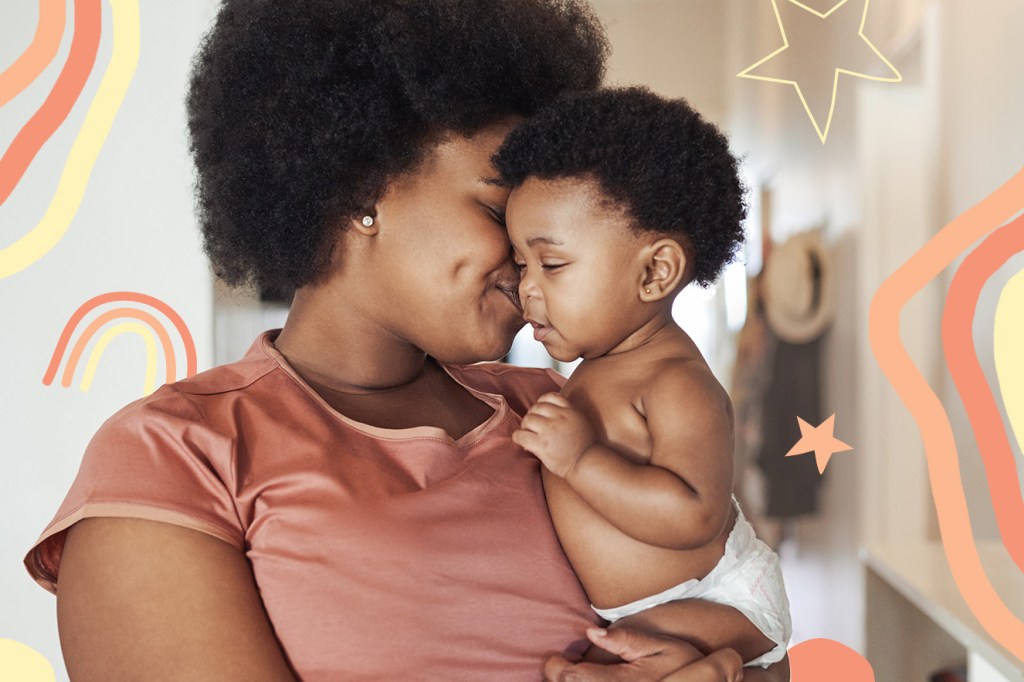 mulher negra com o cabelo black powe carregando bebê também negro, usando apenas fralda. Ela veste uma camiseta rosa e sorri enquanto encosta o rosto no do bebê.