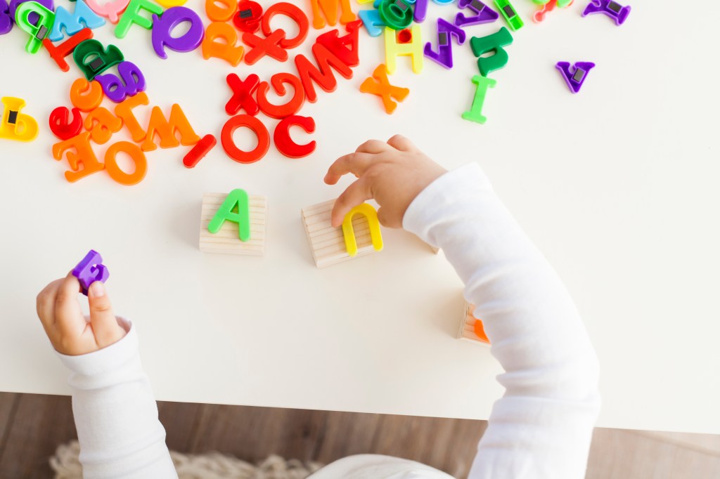 Criança pequena brincando com letras coloridas sobre uma mesa branca.