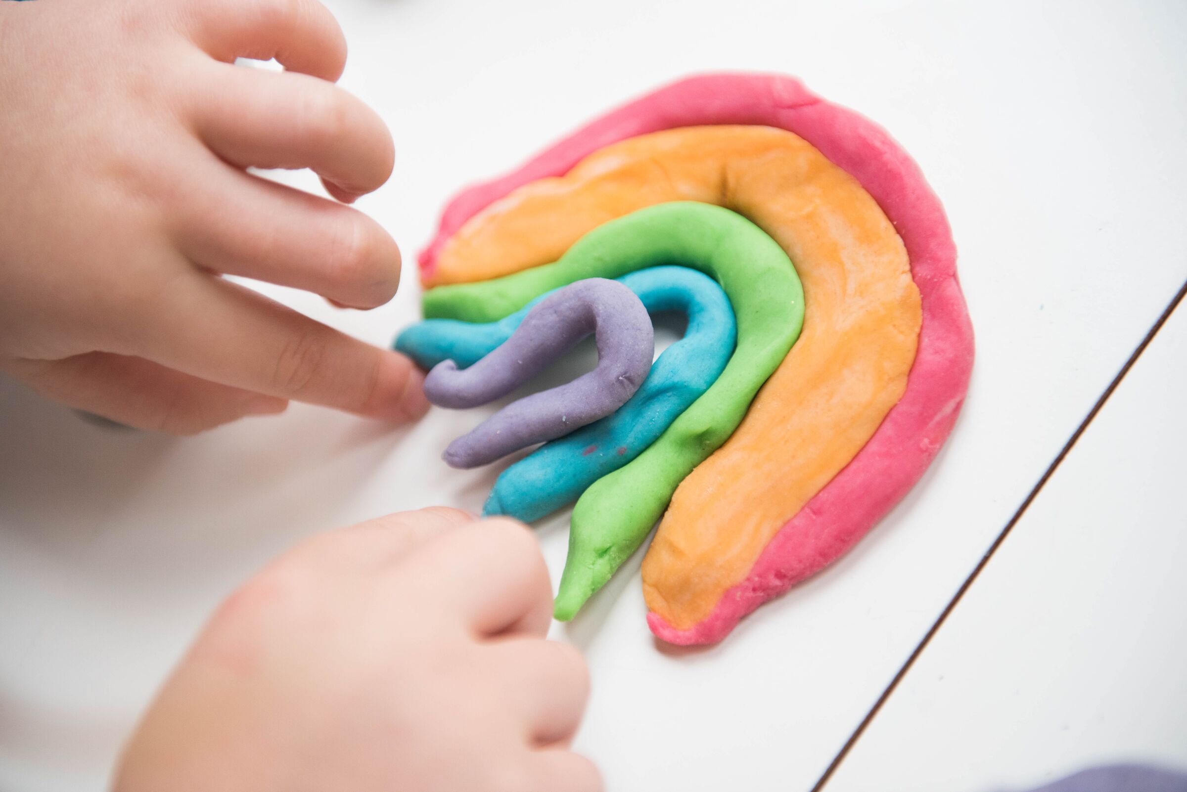 Mãos infantis brincando com massinhas coloridas.