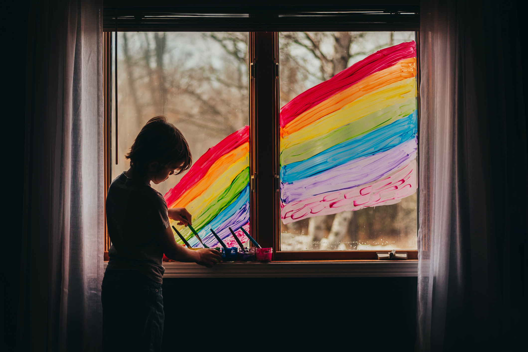 Criança pintando arco-íris na janela
