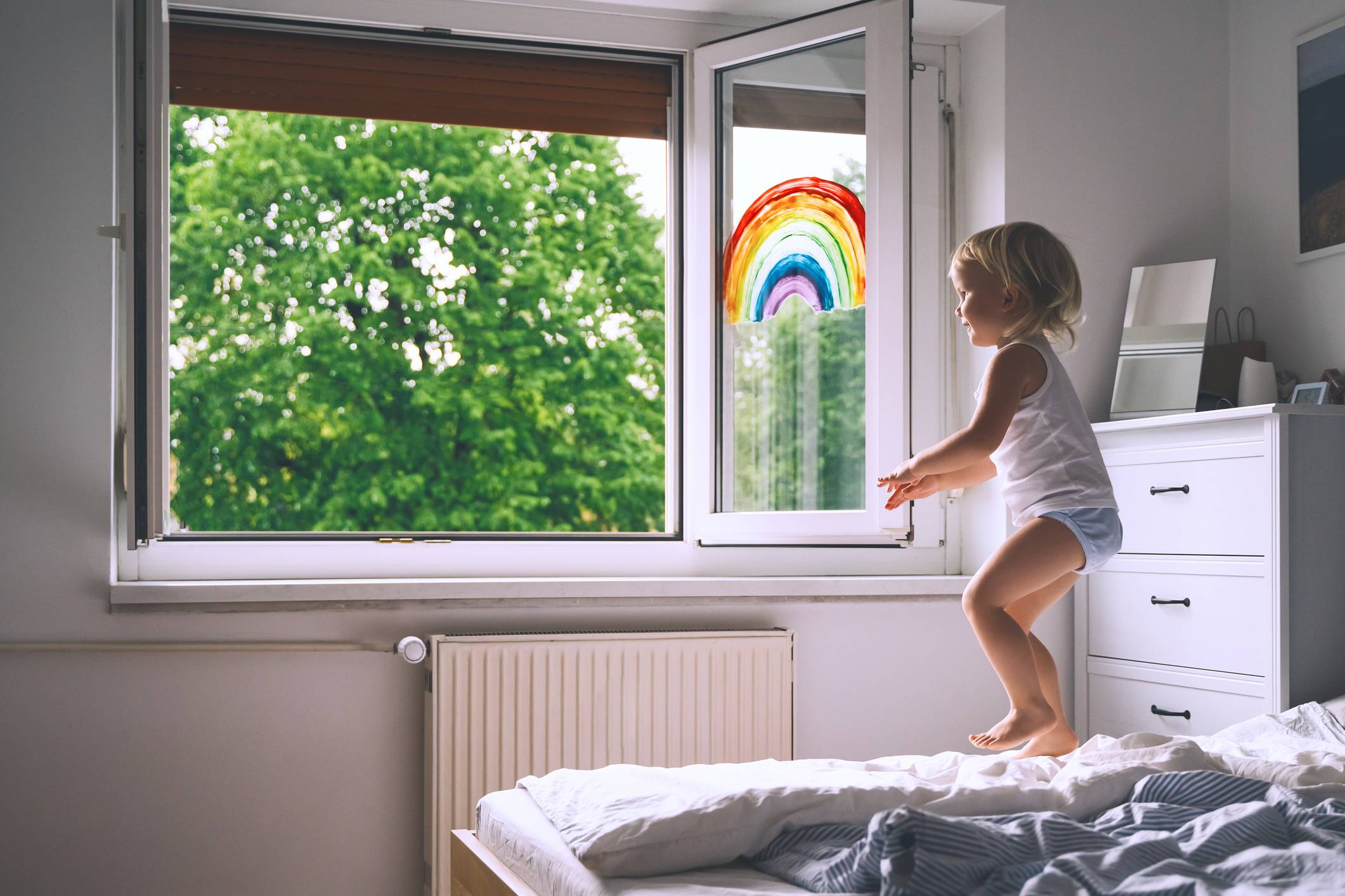 Menina pulando na cama com arco-íris desenhado na janela