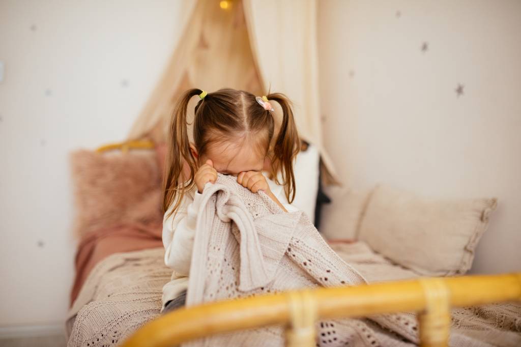 Menina sentada na cama cobrindo o rosto