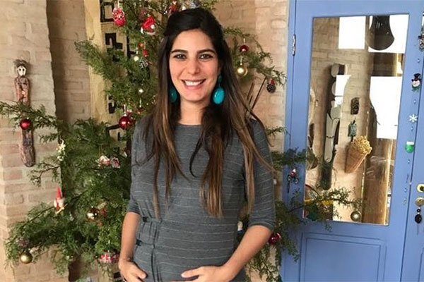 Andreia Sadi grávida e sorrindo diante de uma árvore de Natal