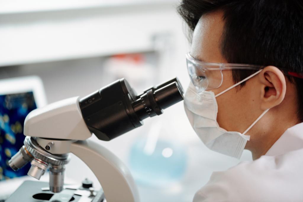 Cientista homem, branco de cabelo castanho, no laboratório olhando pelo microscópio