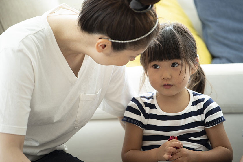 mulher, sentada ao lado de uma menina, conversa com a criança