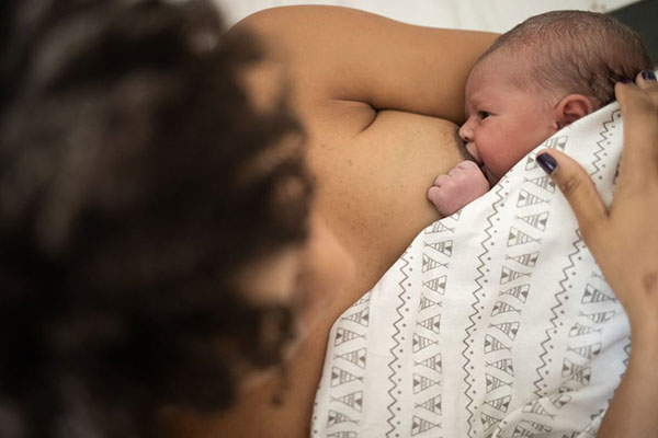 Mulher amamenta bebê coberta com uma manta