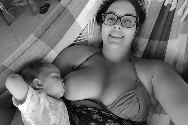 mãe deitada em uma rede amamentando uma bebê