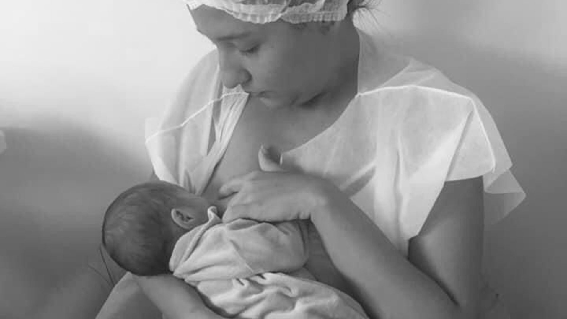 mãe com avental e touca de hospital amamentando bebê no colo
