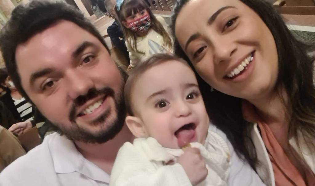 Fernando, Benício e Flávia, Benício no meio dos dois, sorrindo.