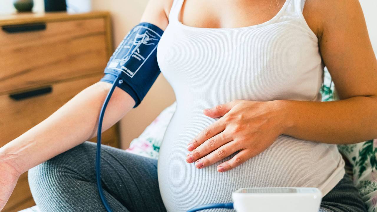 close na barriga de uma grávida que está com um aparelho de medir pressão envolto em seu braço
