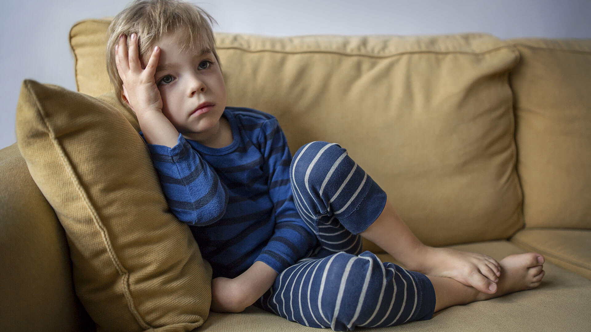 garoto sentado em um sofá com a mão na cabeça e semblante de desânimo