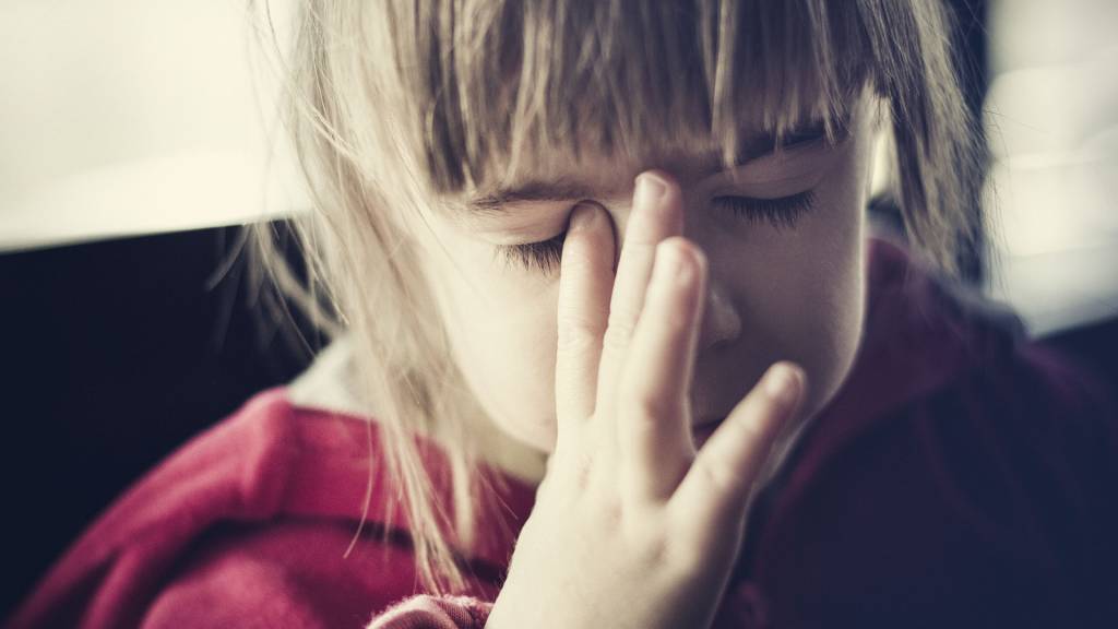 close no rosto de uma menina, que está de olhos fechados e com uma das mãos na lateral do nariz