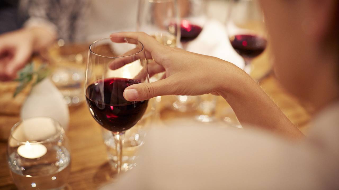mão de mulher em uma taça de vinho sobre uma mesa cheia de taças