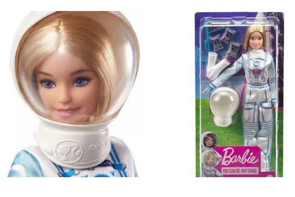 de um lado, o close de uma boneca loira usando um capacete transparente de astronauta. De outro, uma caixa com a parte da frente transparente e com essa mesma boneca dentro. Ela usa um macacão de astronauta