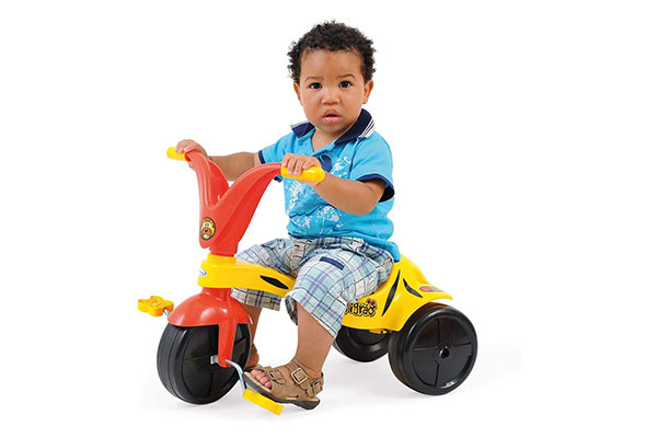 garoto sentado em um triciclo amarelo e laranja, com rodas pretas