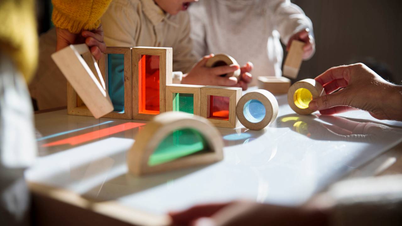 Mesa de escolinha com brinquedos de madeira e crianças brincando