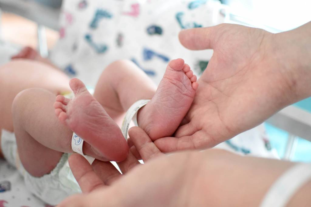 pezinhos do recém-nascido com identificação do hospital apoiados em mãos de adultos