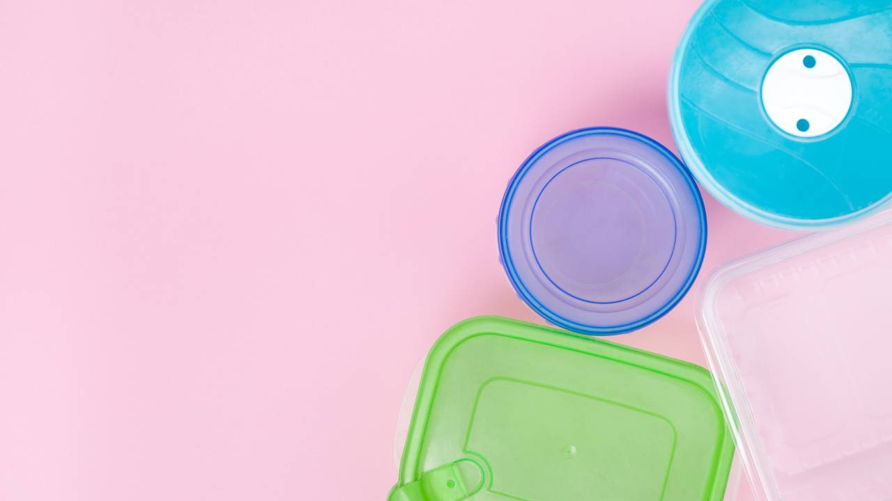 Potes de plástico para armazenar comida, com tampas coloridas (sobre fundo rosa claro).