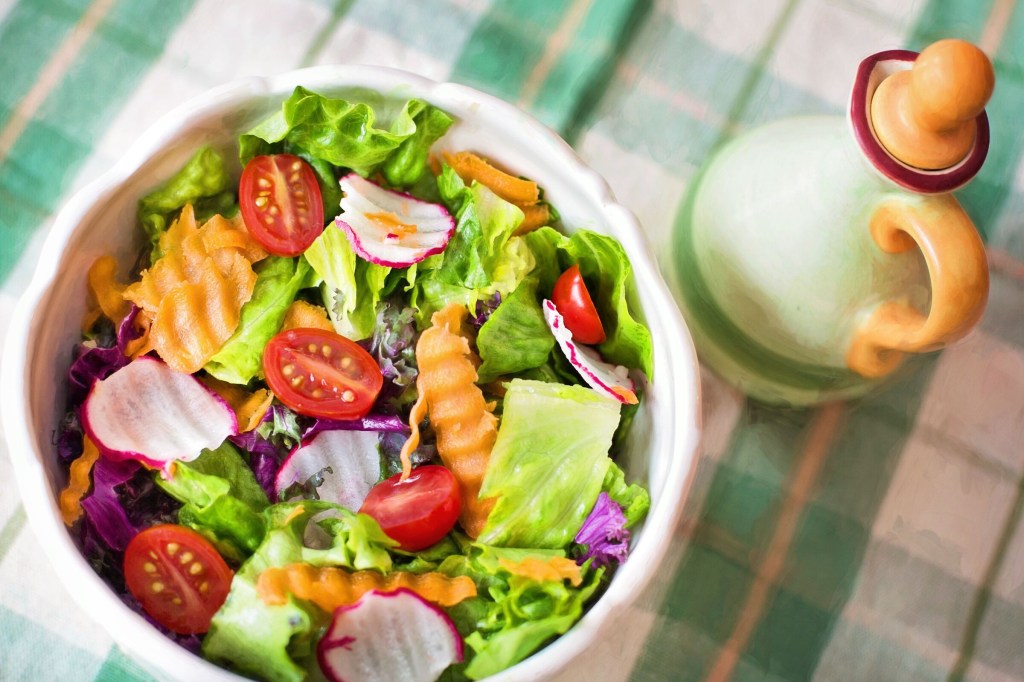 bowl branco de salada sobre uma toalha xadrez verde e branca. A salada é formada por folhas verdes de alface, tomate cereja, cenoura e rabanete.
