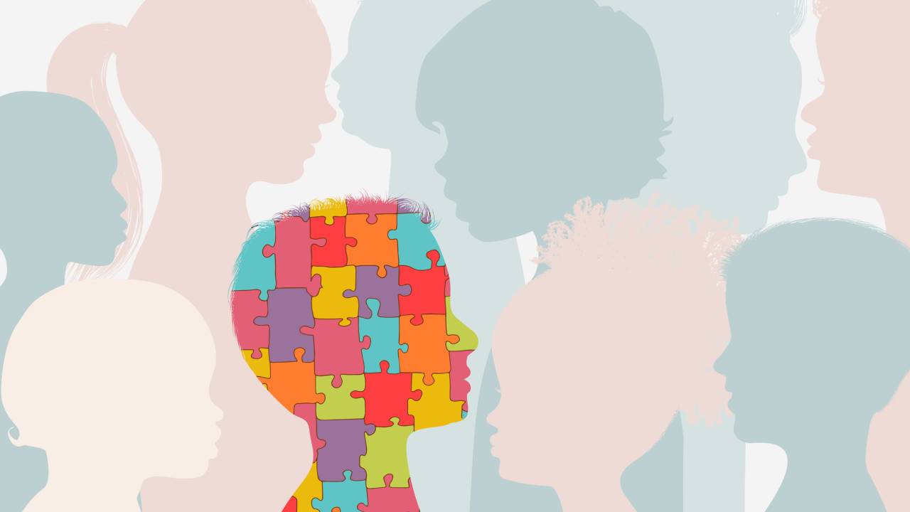 Ilustração de crianças de perfil em tons pasteis azul e rosa. Um desses perfis está em destaque, com formado por peças de quebra-cabeça coloridas, símbolo do autismo.