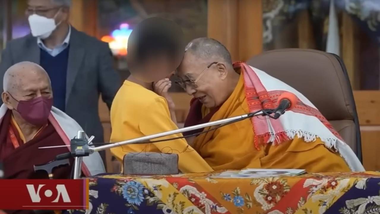 Dalai Lama com a cabeça encostada na de um menino. Ele segura seu queixo.