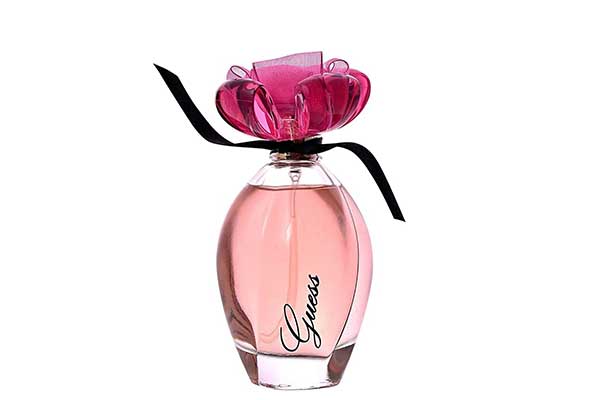 frasco de vidro de perfume transparente e em formato arredondado. Dentro dele, há um líquido rosado. A tampa tem formato de flor