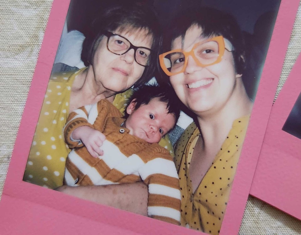 foto de uma senhora, uma mulher, ambas de óculos e bem parecidas. Entre elas está um bebê