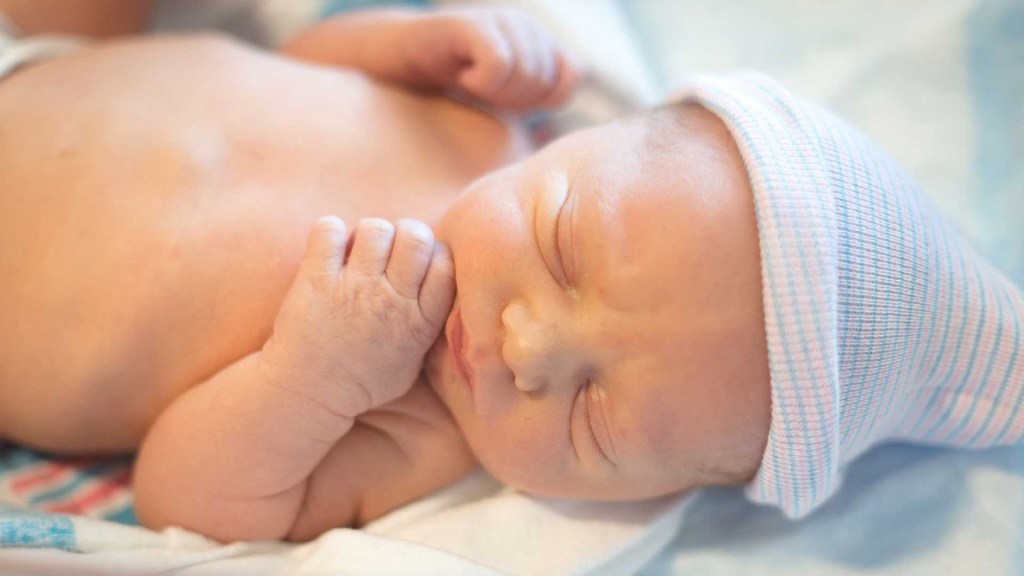 bebê recém-nascido com olhos fechados, deitado e usando uma touca