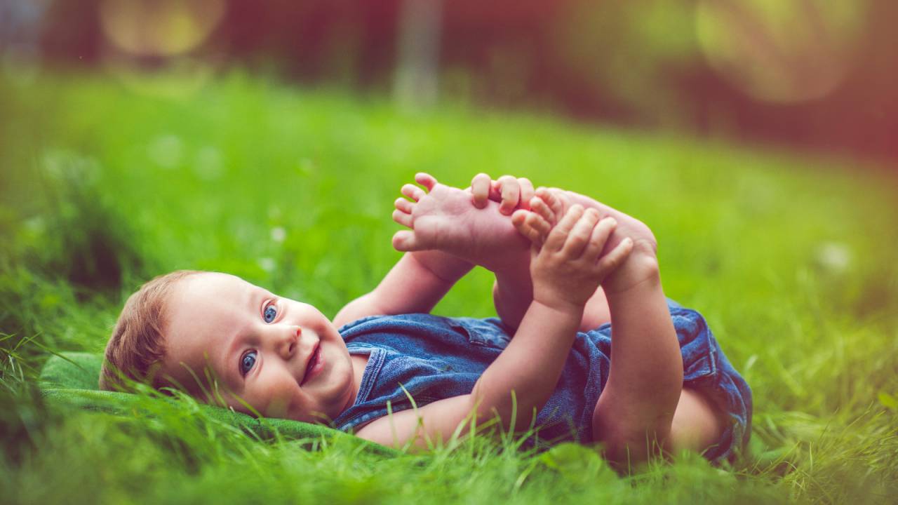 Bebê segurando pezinho deitado na grama