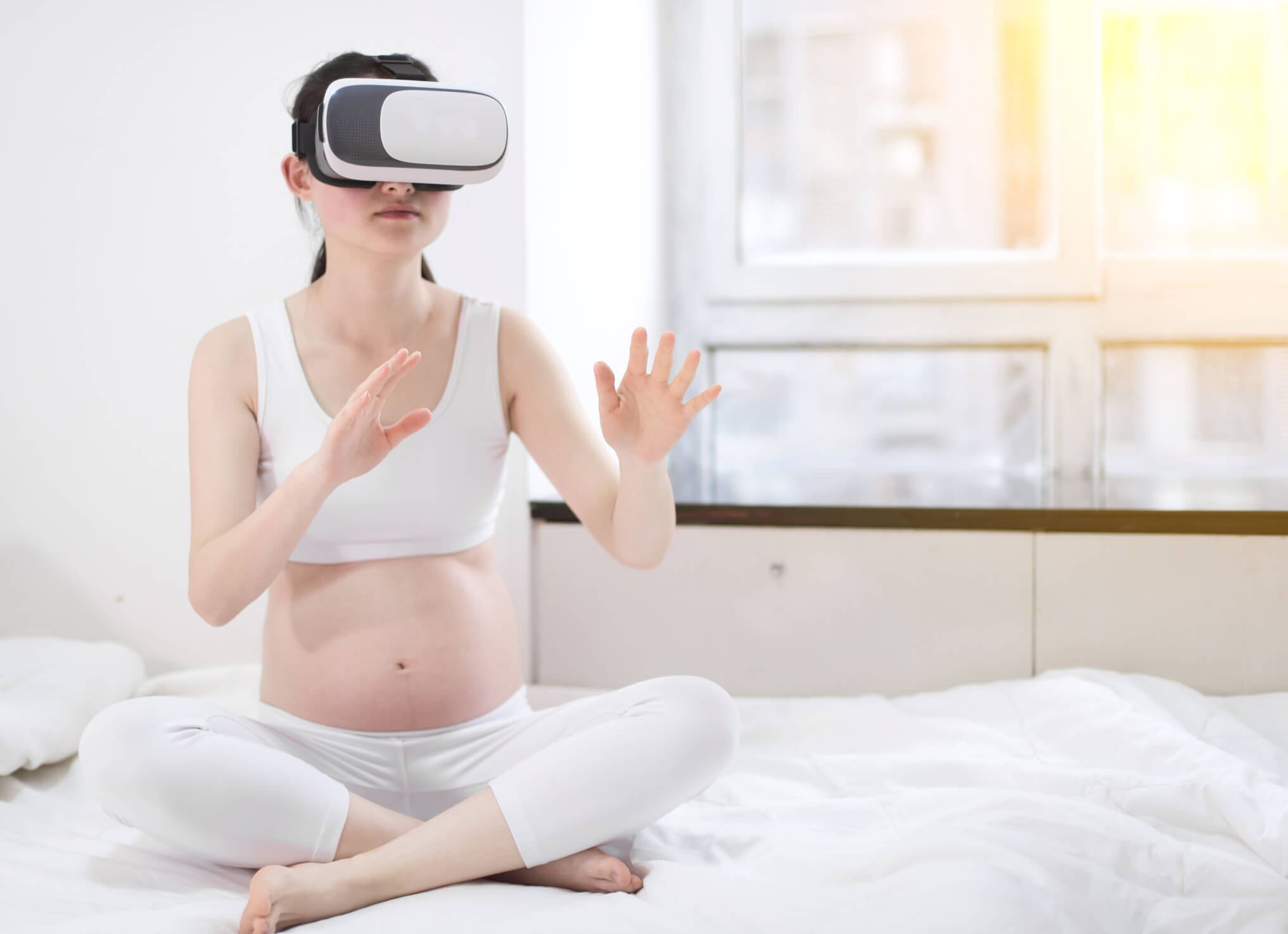 Mulher grávida sentada na cama usando óculos de realidade virtual.