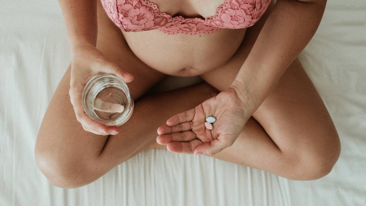mulher gravida sentada com copo de agua e remedios na mao