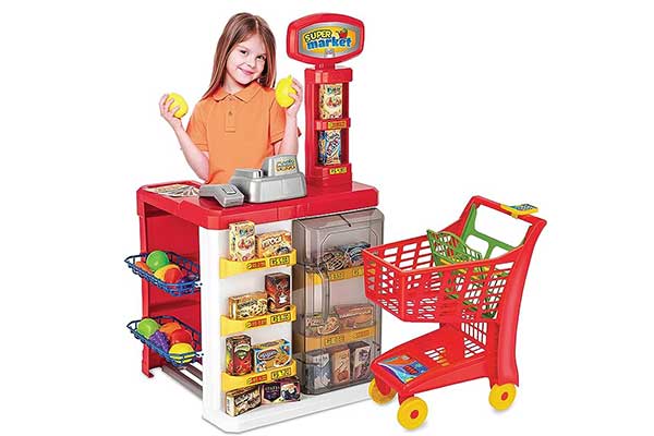 menina brincando com um brinquedo que simula um caixa de supermercado. Na frente, há um carrinho de mercado, também de brinquedo